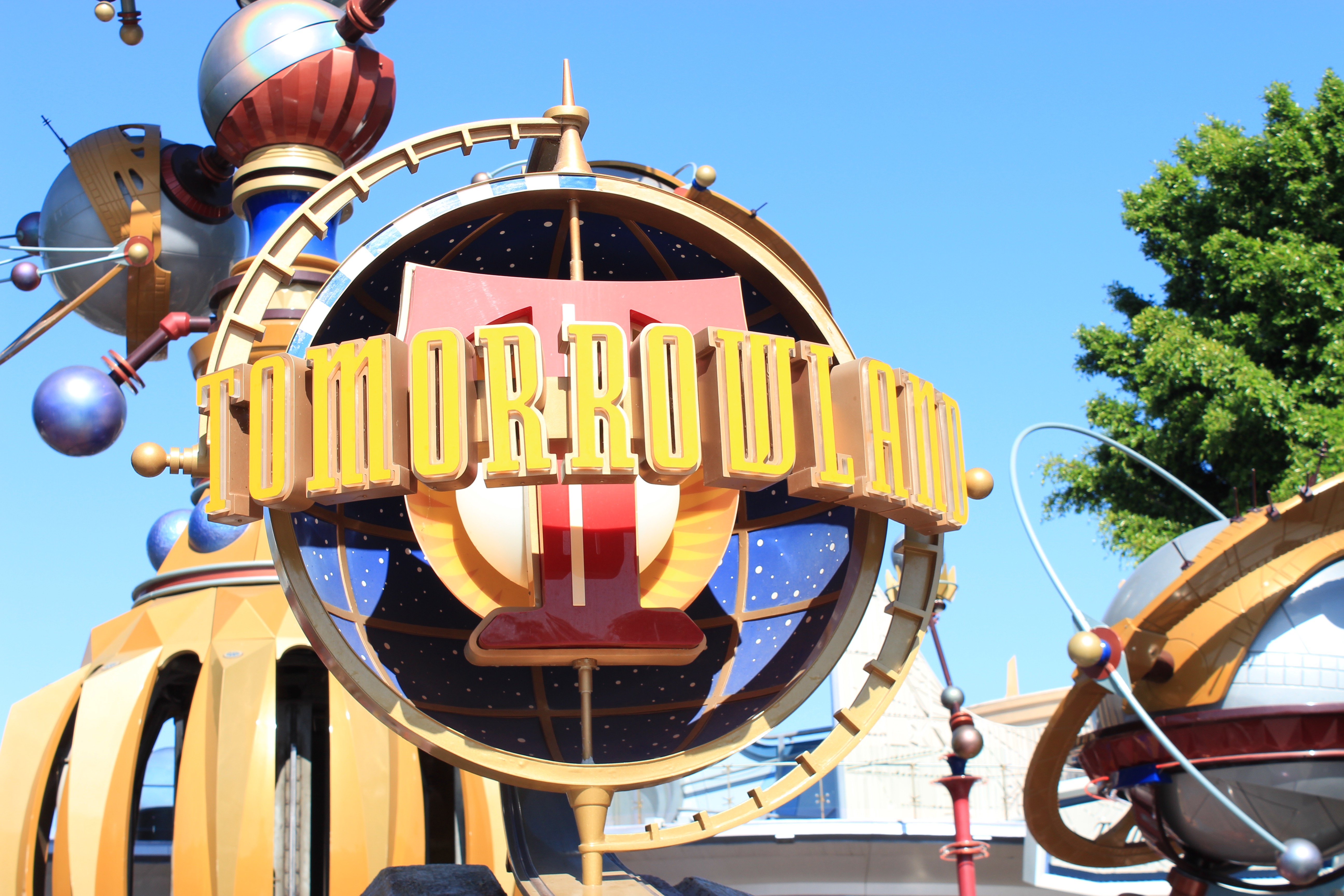 The sign outside of Tomorrowland with the Tomorrowland logo and the Astro Orbitor in the background.