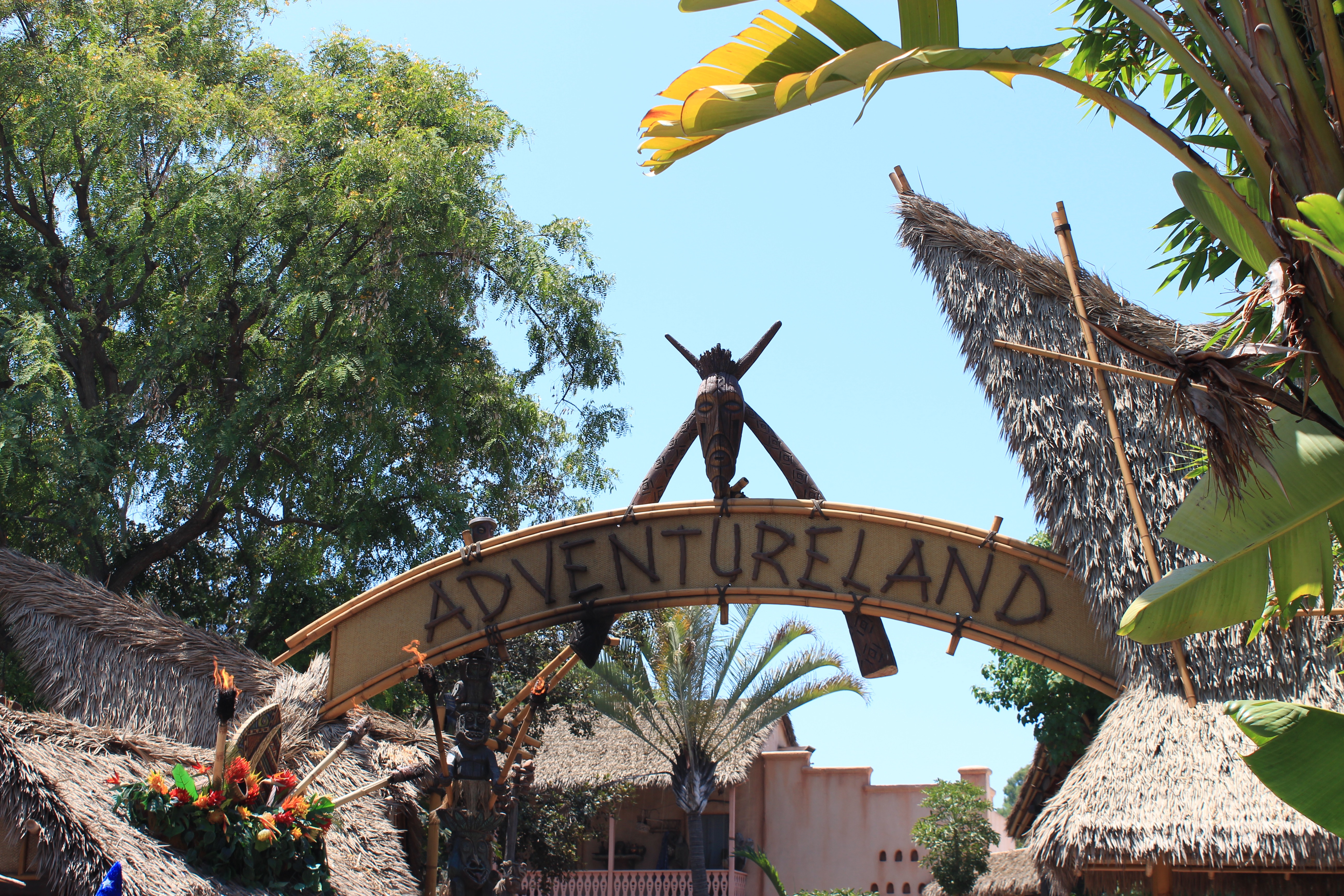 Sign over the entryway to Adventureland with tiki torches and "Adventureland" written in large letters.